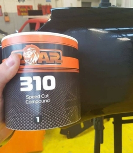 Hand holding a tin of speed cut compound beside a glossy car