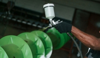 Gloved hand spray-painting green parts with a spray gun