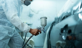 Painter in a protective suit spray-finishing a car