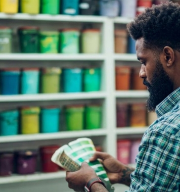 Customer comparing paint colour swatches in front of shelves of paint tins