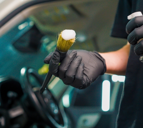 Gloved hand holding a detailing brush with foam inside a car